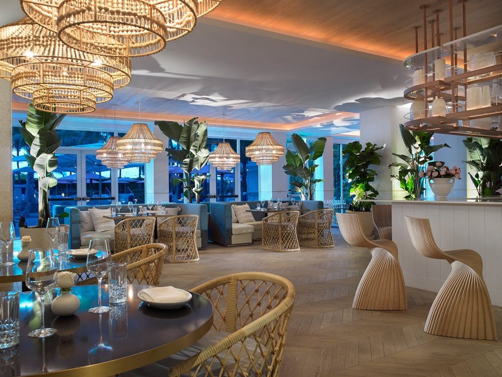 Modern coastal venue interior with woven chandeliers, tropical plants, and elegant seating overlooking ocean views