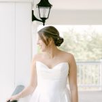 Chelsea smiling in her strapless wedding gown with low updo hairstyle on a covered porch