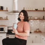 Wedding photographer sitting on kitchen counter holding coffee mug with camera nearby
