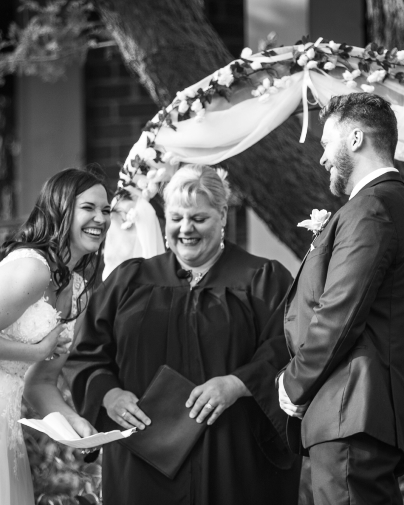 Wedding officiant conducting a joyful outdoor ceremony under a floral arch with laughing bride and groom in Savannah