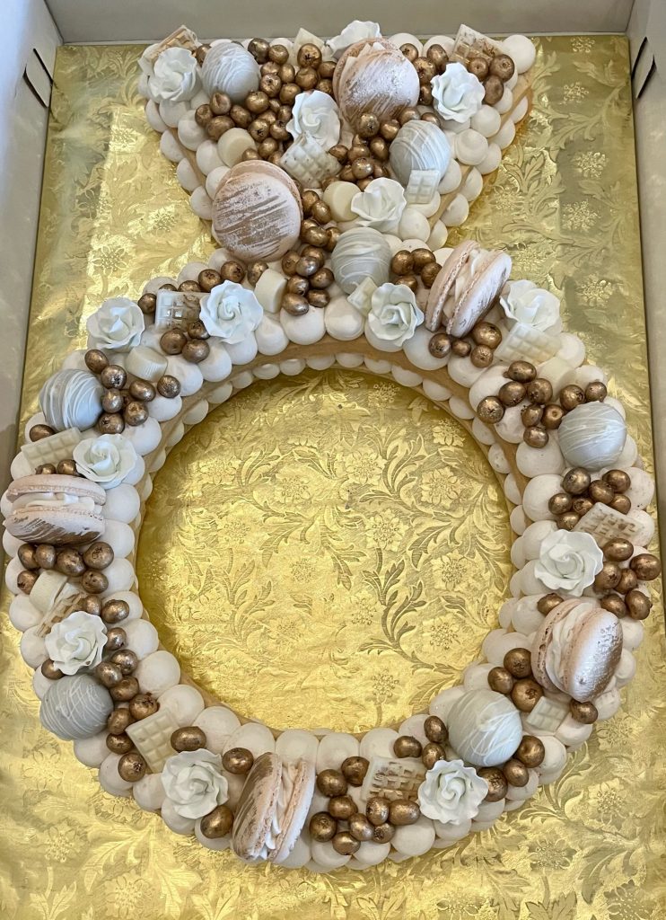 Letter B-shaped dessert board decorated with white and gold macarons, meringues, and sugar flowers