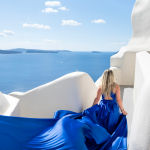 Woman in flowing royal blue dress on white Santorini terrace overlooking Aegean Sea, exemplifying destination wedding elegance