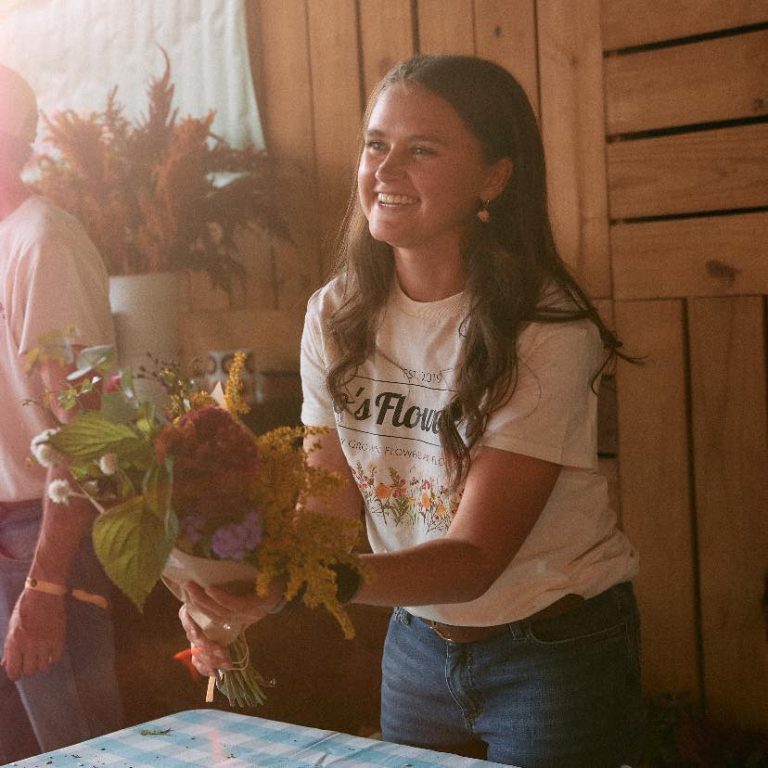 Smiling woman holding colorful bouquet at flower workshop table
