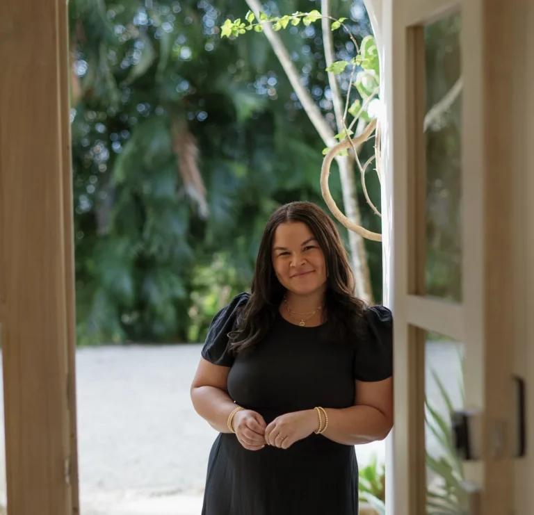 Woman in black dress smiling while standing in doorway with natural light