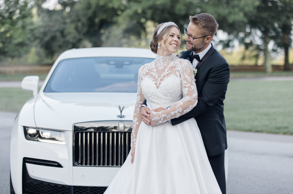Bride and groom embracing beside white luxury wedding car in Charlotte
