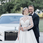 Bride and groom embracing in front of white Rolls-Royce luxury wedding vehicle