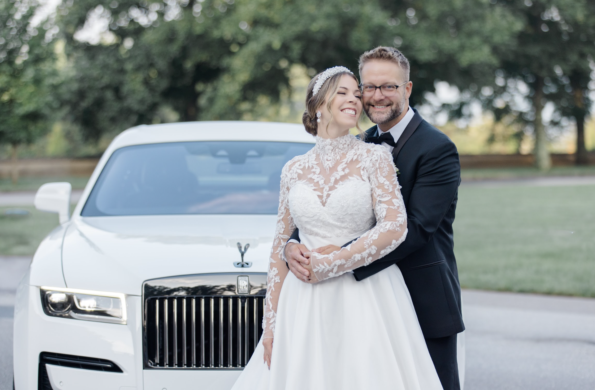 Bride and groom embracing in front of white Rolls-Royce luxury wedding vehicle