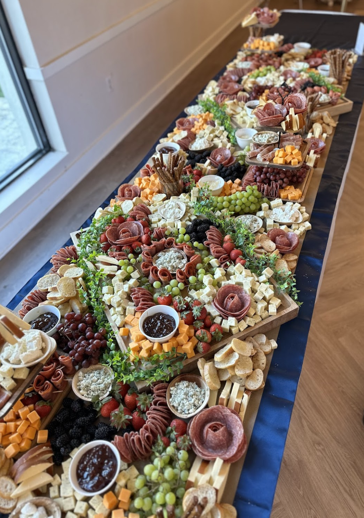 Elaborate charcuterie grazing table with meats, cheeses, fruits, crackers, and decorative salami roses