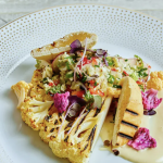 Artfully plated grilled cauliflower steak with colorful vegetables and edible flowers on gold-dotted china
