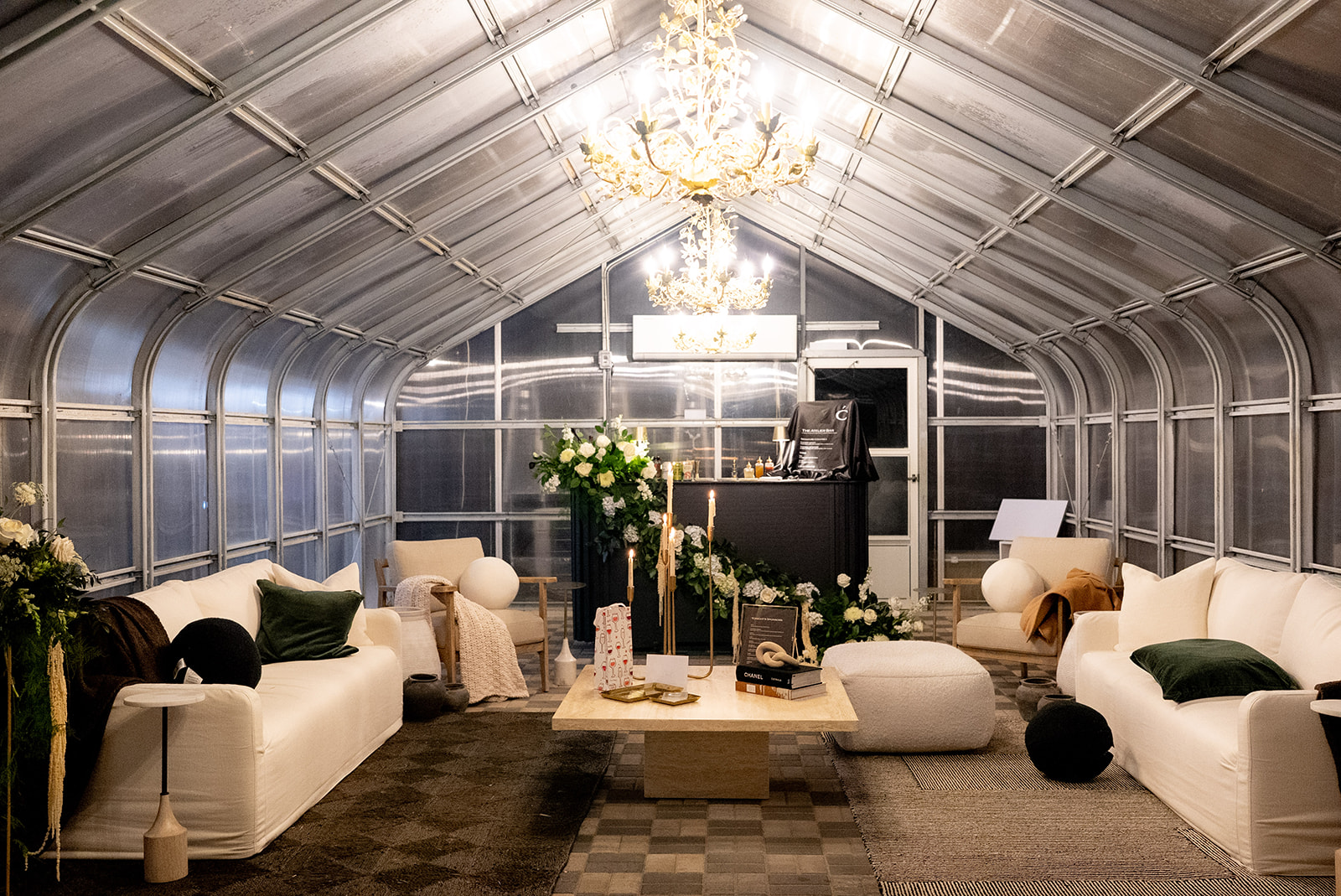 Greenhouse lounge space with vaulted ceiling, chandelier lighting, and modern white seating