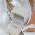 Diamond engagement ring in white velvet box surrounded by bridal shoes and pearl accessories