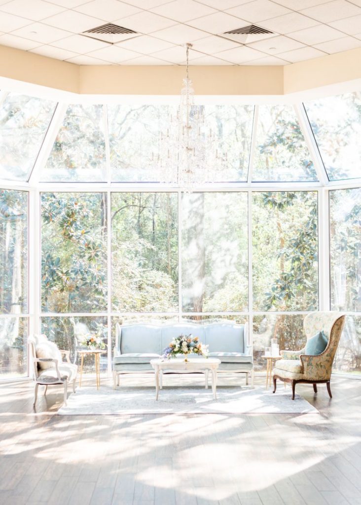 Elegant lounge area with blue velvet sofa and vintage chairs in sunlit glass-walled room