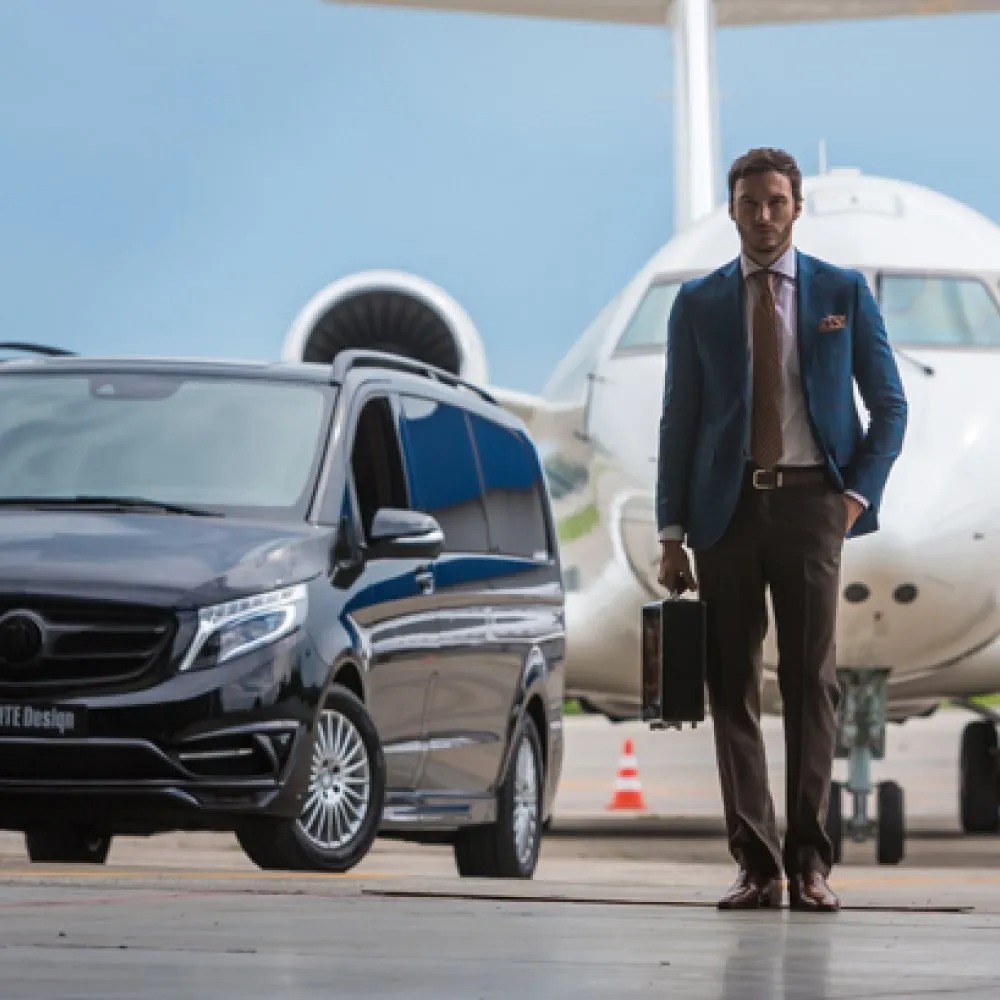 black transportation van and airplane in the background of man walking away with briefcase