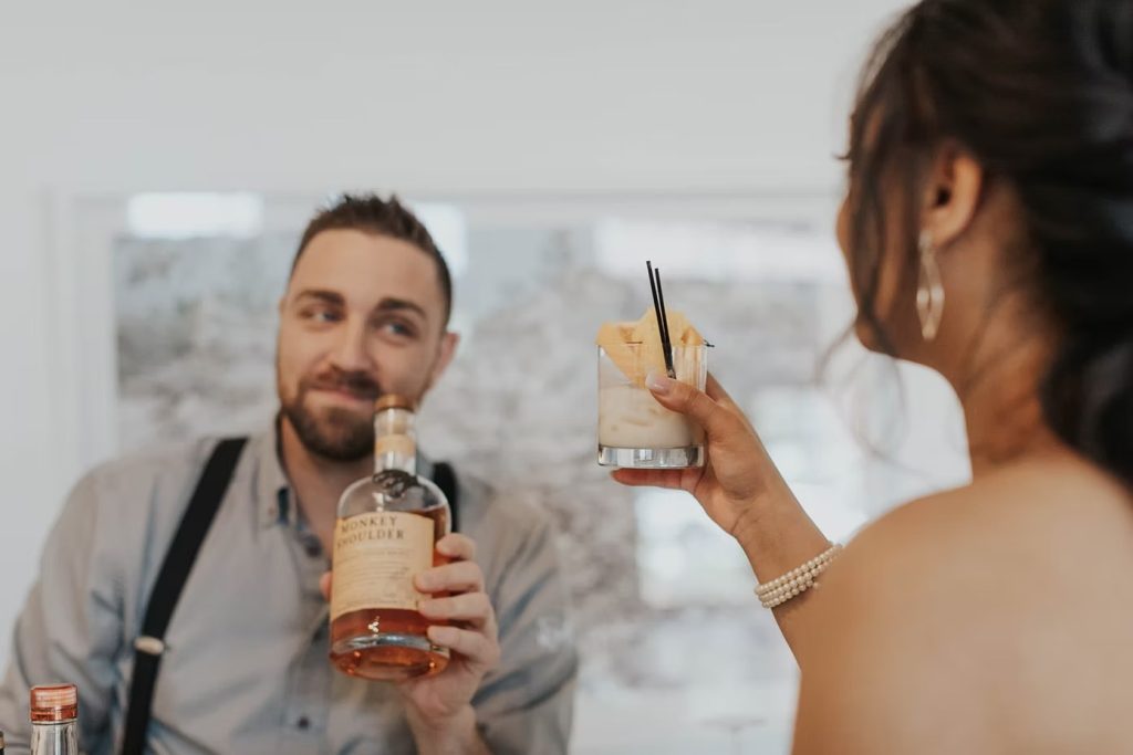 Bartender serving cocktail garnished with citrus to wedding guest in pearl bracelet