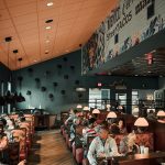 Casual restaurant interior with teal walls, orange ceiling, and diners seated in booths under pendant lights