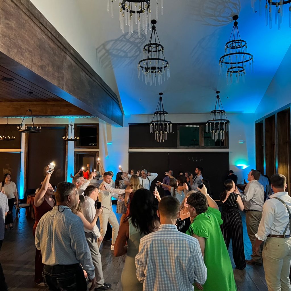 Wedding guests dancing under blue uplighting and crystal chandeliers in modern Colorado reception venue