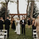 Bride and groom walking down aisle after outdoor ceremony under wooden arbor with pine trees and guests