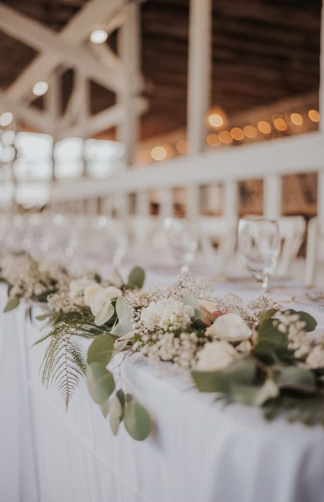 White floral garland with eucalyptus, ferns, and baby's breath adorning reception table at rustic barn wedding venue