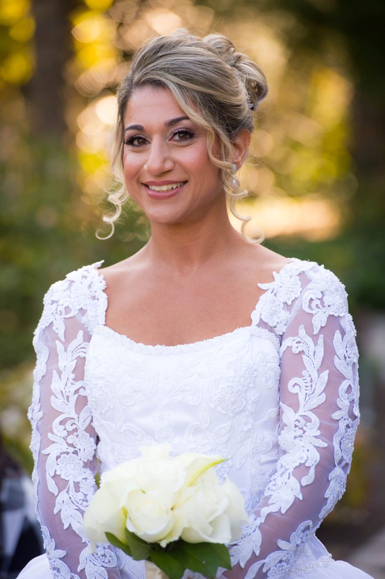 Smiling bride with upswept blonde hair wearing white lace wedding dress with illusion sleeves