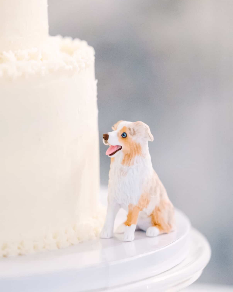 white two tiered cake with white and brown dog figurine on the side
