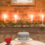 light blue small cake with white details on a white cake stand with brick wall and candlelit