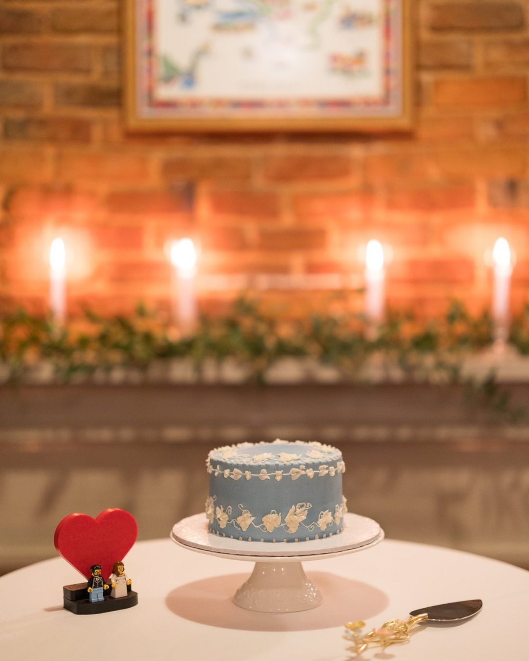 light blue small cake with white details on a white cake stand with brick wall and candlelit