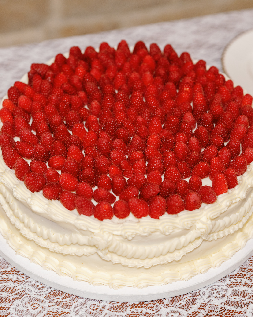 white cake with piping details with raspberries covering the top