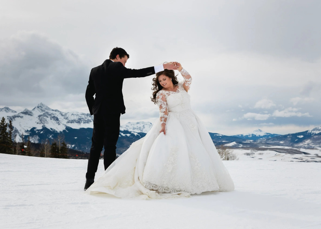 Bride and groom dancing in snowy mountain landscape
