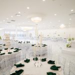 Modern white ballroom with clear chiavari chairs and emerald green napkins