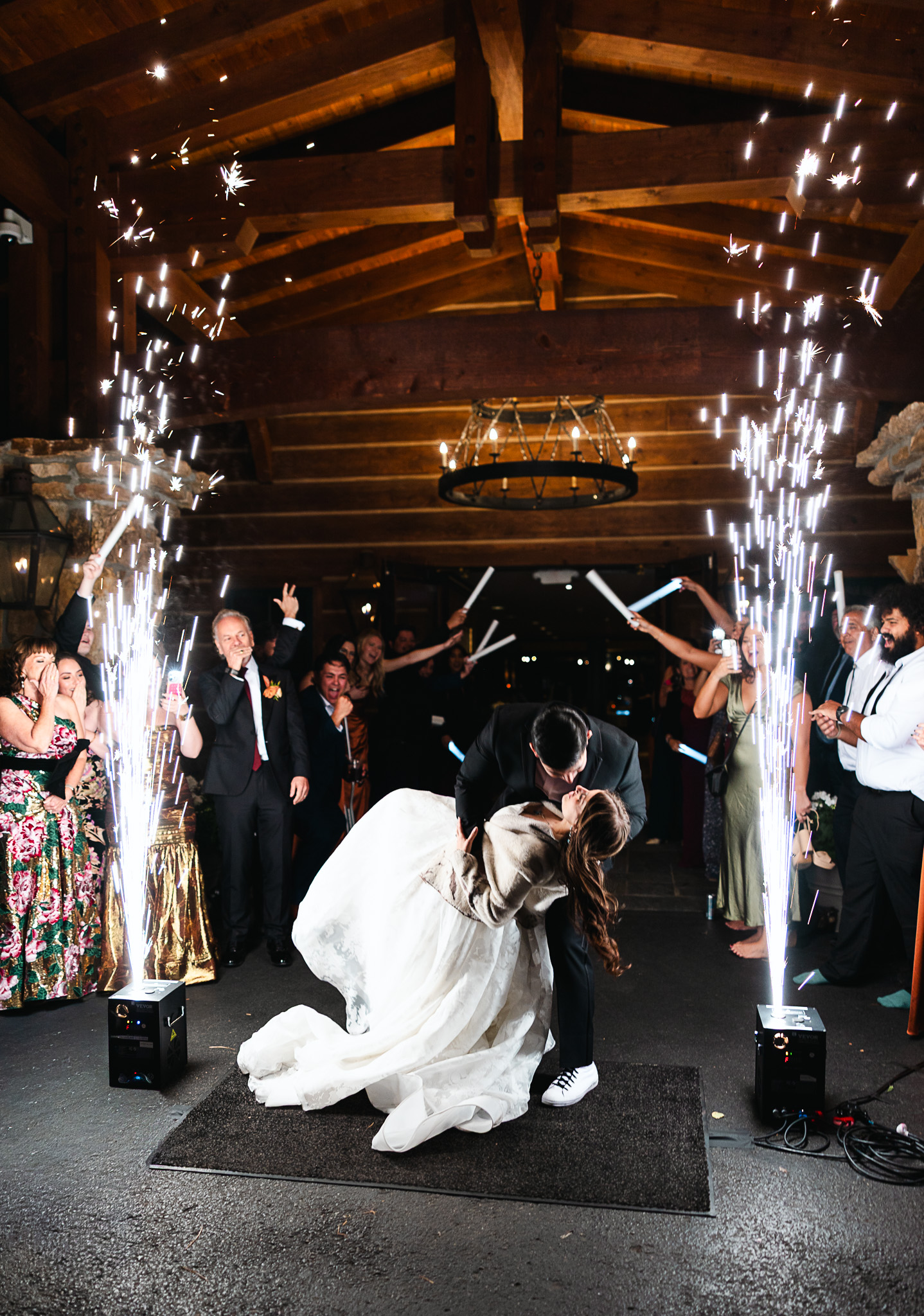 Newlyweds dip and kiss between sparkler fountains during rustic barn reception