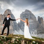 Bride and groom holding hands on mountain ridge with dramatic Dolomites peaks behind them