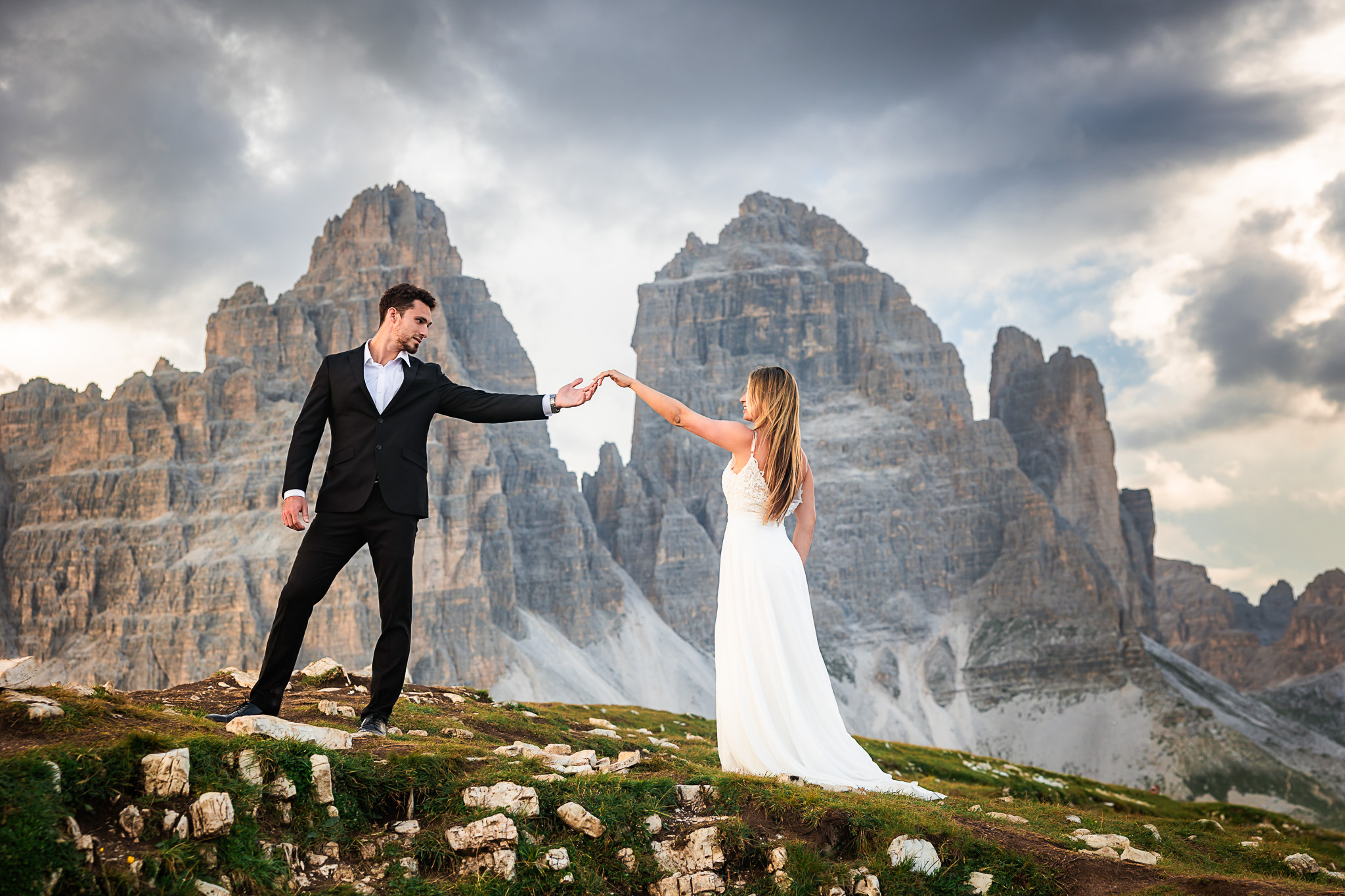 Bride and groom holding hands on mountain ridge with dramatic Dolomites peaks behind them