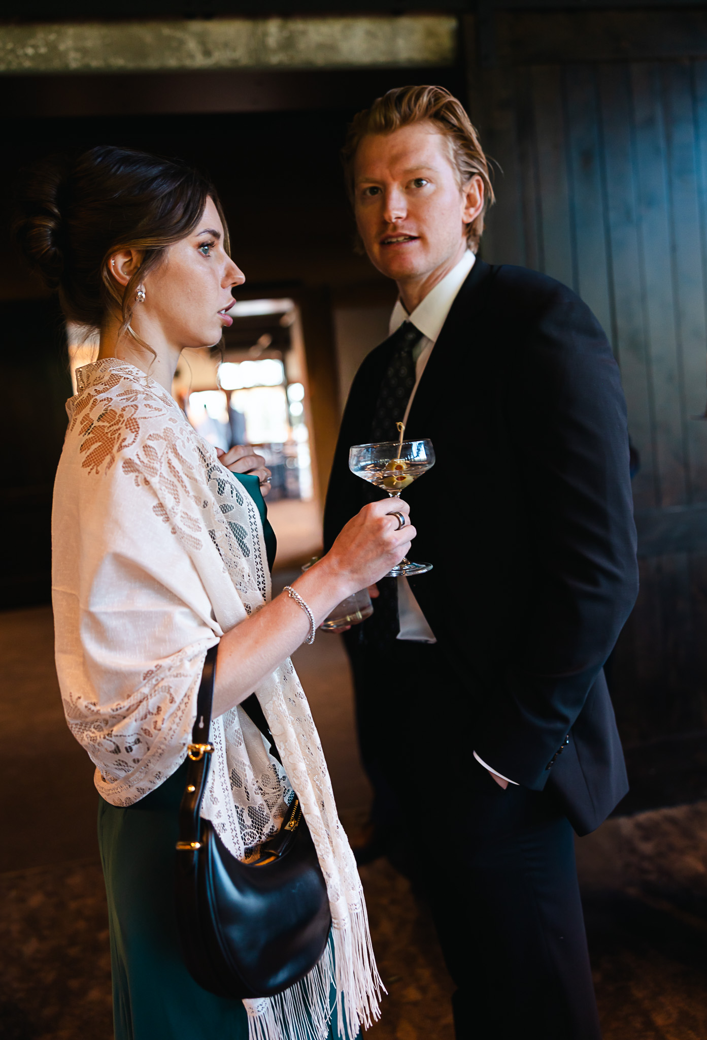 Bride in lace shawl and groom in navy suit share champagne at elegant reception