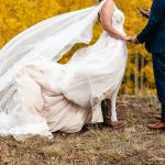 Bride and groom holding hands in autumn forest, bride's veil and gown flowing in the breeze against golden aspen trees