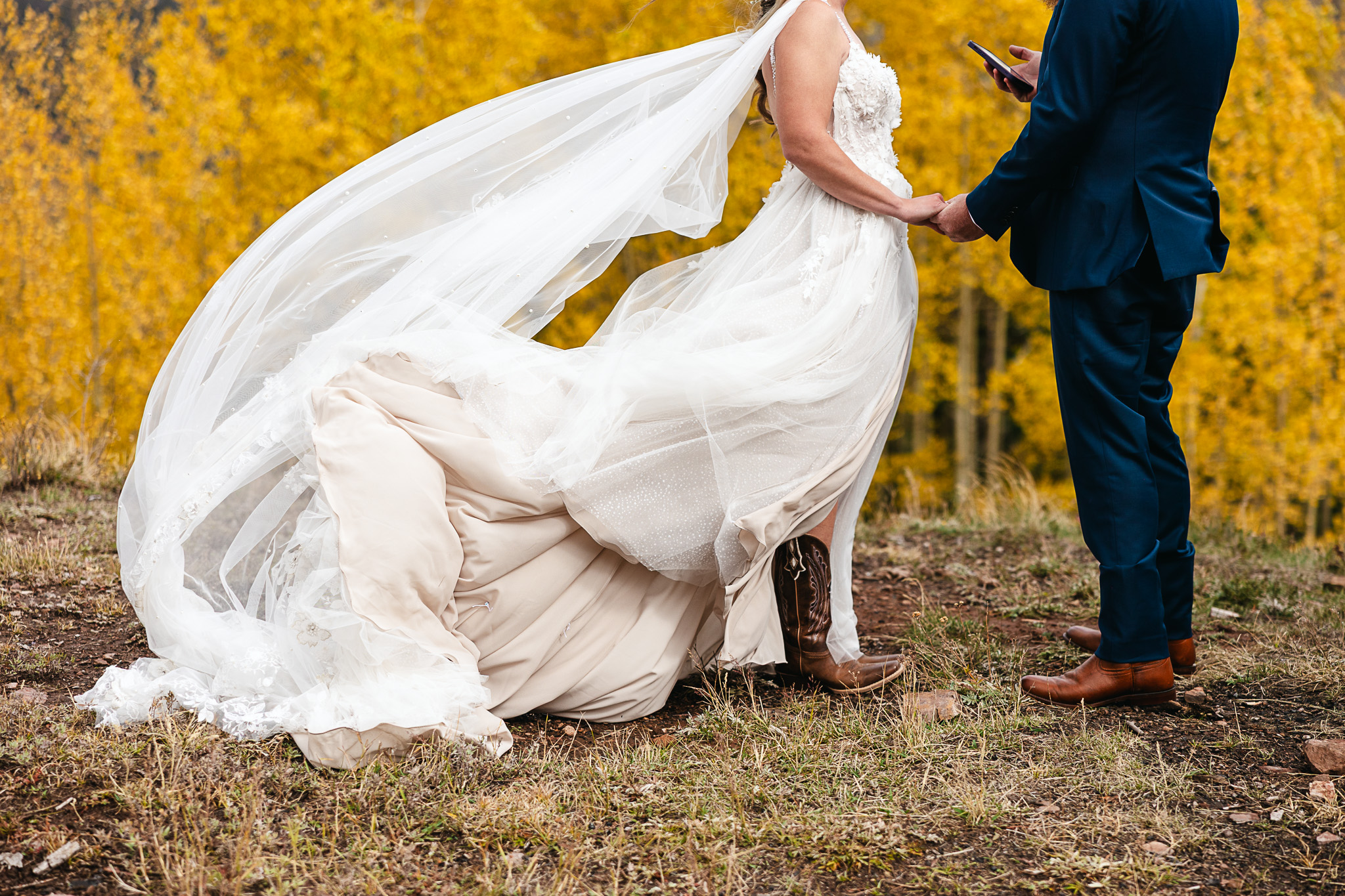 Bride and groom holding hands in autumn forest, bride's veil and gown flowing in the breeze against golden aspen trees