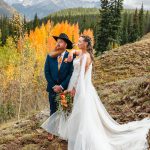 Bride and groom posing on mountainside with vibrant fall aspens and snow-capped peaks in Greater Denver Area