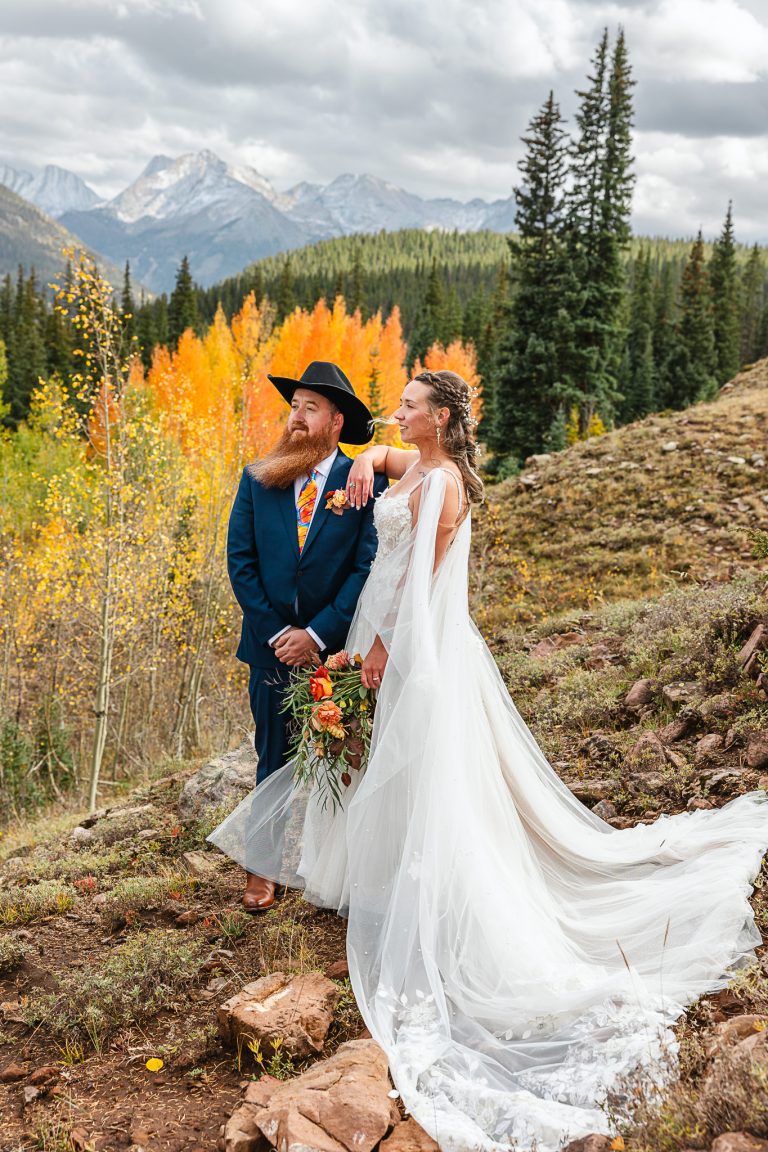 Bride and groom posing on mountainside with vibrant fall aspens and snow-capped peaks in Greater Denver Area