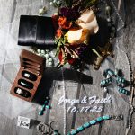 Overhead view of wedding preparation items including bridal bouquet with roses, jewelry, perfume, and accessories arranged on dark surface