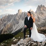 Bride and groom posing on alpine mountaintop with dramatic Dolomite peaks in the background