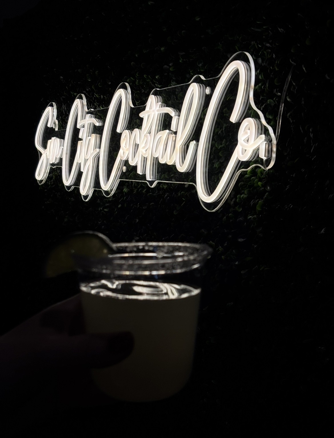 White neon "Cocktails" sign glowing above cocktail glasses at Sun City Cocktail Co. mobile bar setup