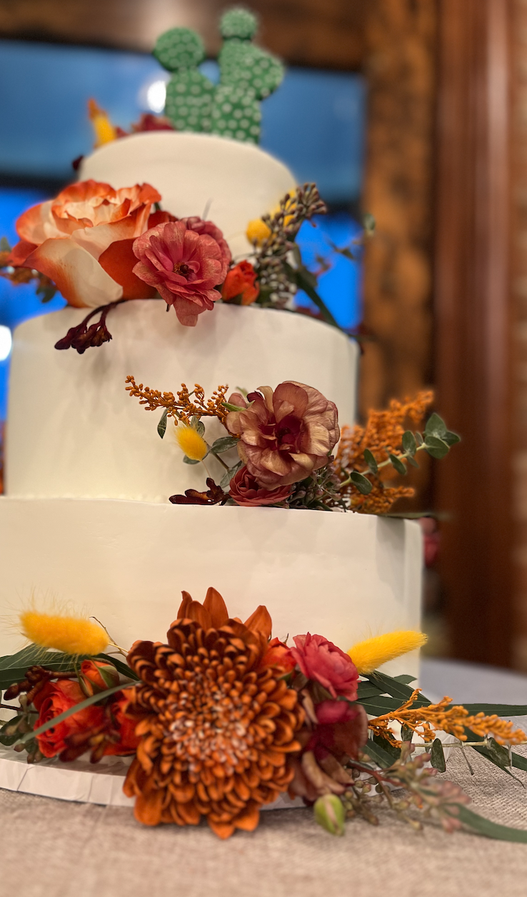 Three-tier white wedding cake decorated with fall flowers in burgundy and orange tones