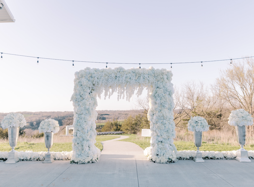 Elegant white floral ceremony arch with matching arrangements overlooking Iowa countryside