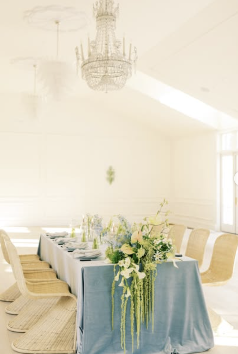Elegant wedding reception table with dusty blue runner, cascading floral centerpiece, and crystal chandelier overhead