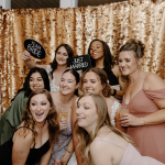 Bridesmaids celebrating at photo booth with gold sequin backdrop holding Team Bride and Just Married signs