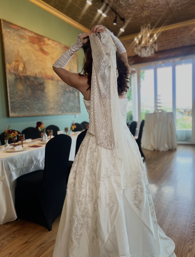 Bride in beaded wedding gown at Sunset Parlor reception hall with exposed brick, chandeliers, and elegantly set tables