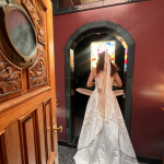 Bride in white gown standing in ornate Victorian doorway with wooden furniture