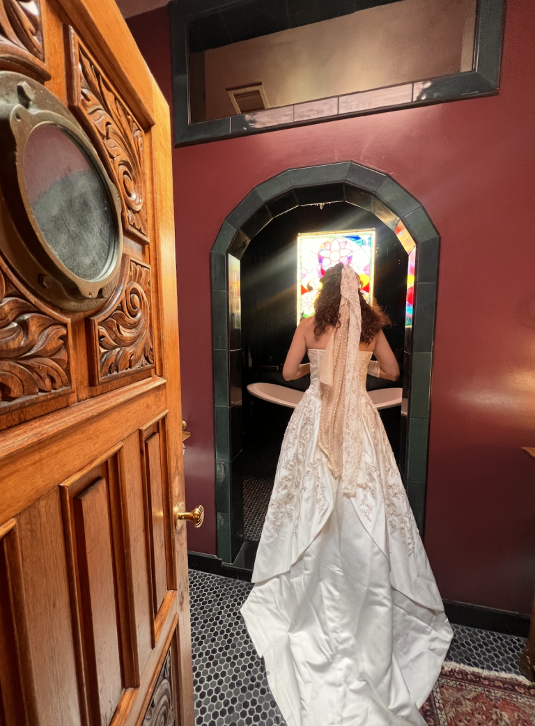 Bride in white gown standing in ornate Victorian doorway with wooden furniture