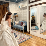 Bride in lace wedding gown admiring her reflection in elegant bridal suite with vintage blue settee and damask wallpaper