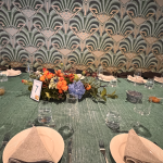 Art Deco wedding reception table with green sequin linens, colorful floral centerpiece, and geometric fan-patterned backdrop