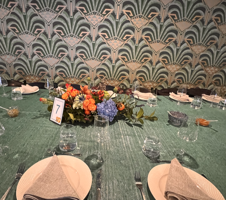 Art Deco wedding reception table with green sequin linens, colorful floral centerpiece, and geometric fan-patterned backdrop